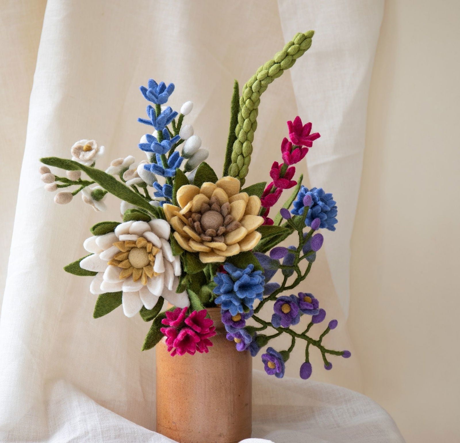 Blumenstrauß Kalpana – Farbenfrohe Filzblumen für stilvolle Dekorationen

Der Blumenstrauß Kalpana ist eine ausdrucksstarke Komposition aus farbenfrohen, handgefertigten Blumen aus Filz von Gry & Sif. Dieser Strauß vereint kräftige Blütenfarben mit zarten Naturtönen – ein harmonisches Zusammenspiel für jede Jahreszeit.
In unserem Filzlig Shop, der sich zu 100 % auf Produkte der Marke Gry & Sif spezialisiert hat, findest du ausschließlich eigens designte Produkte aus Wollfilz, die nachhaltig und unter fairen